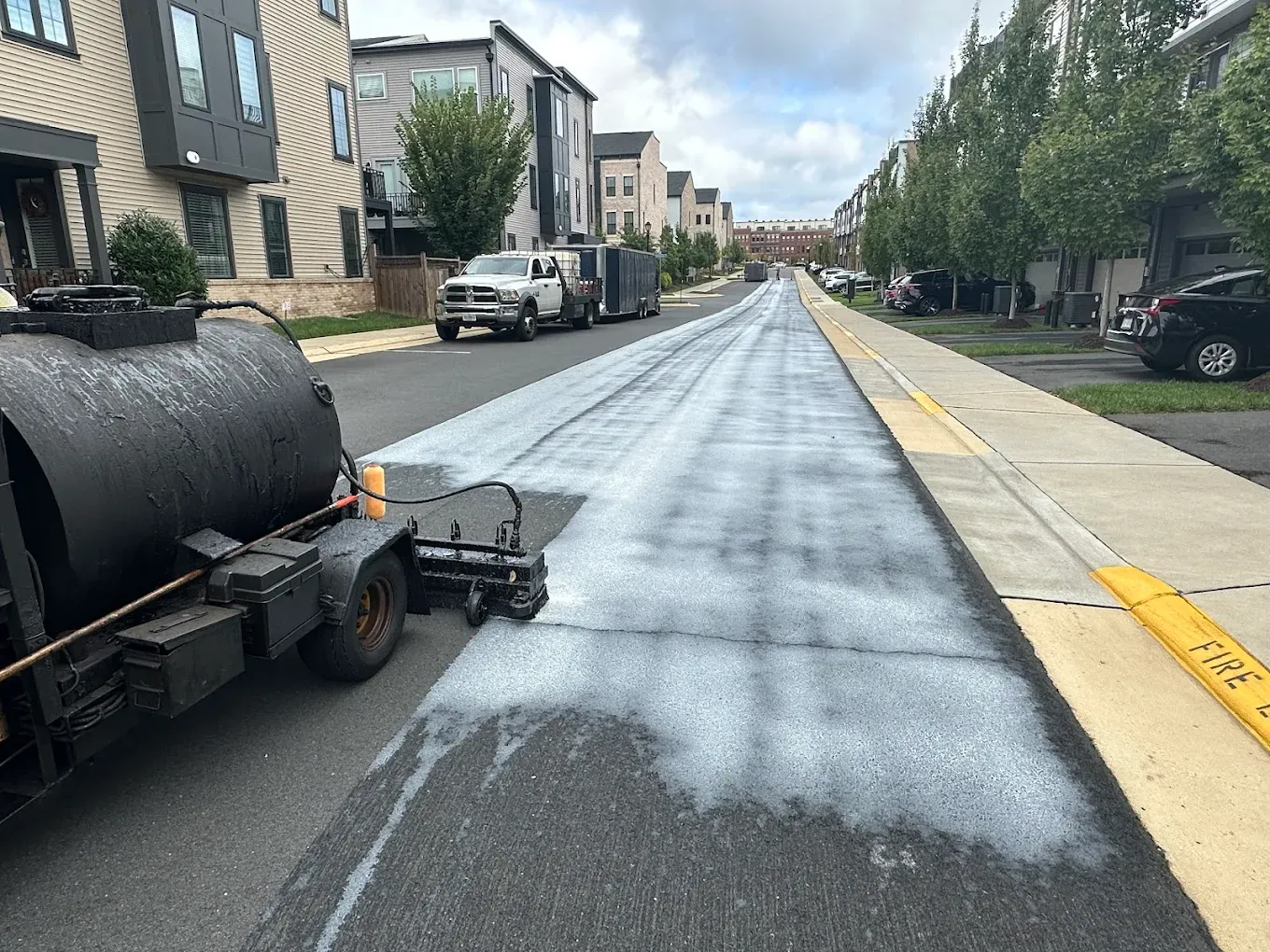 A TriTechnologies spray rig applying Revolution BLACK rejuvenator to a residential street, leaving a white, foamy misted strip that soaks in and cures true black.