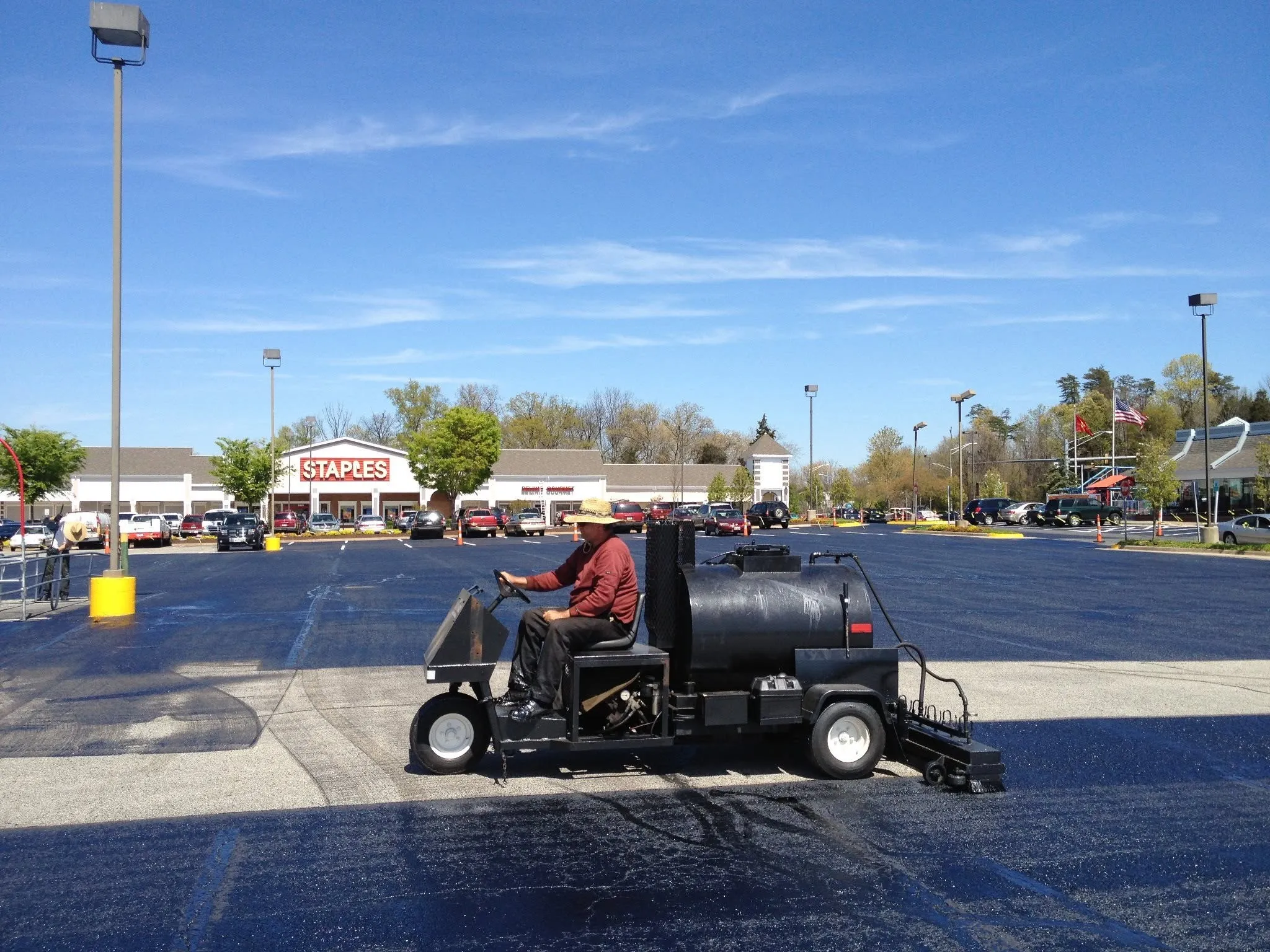 TriTechnologies founder Jeff Pokorny applying asphalt rejuvenator from the spray unit across a shopping-center parking lot.