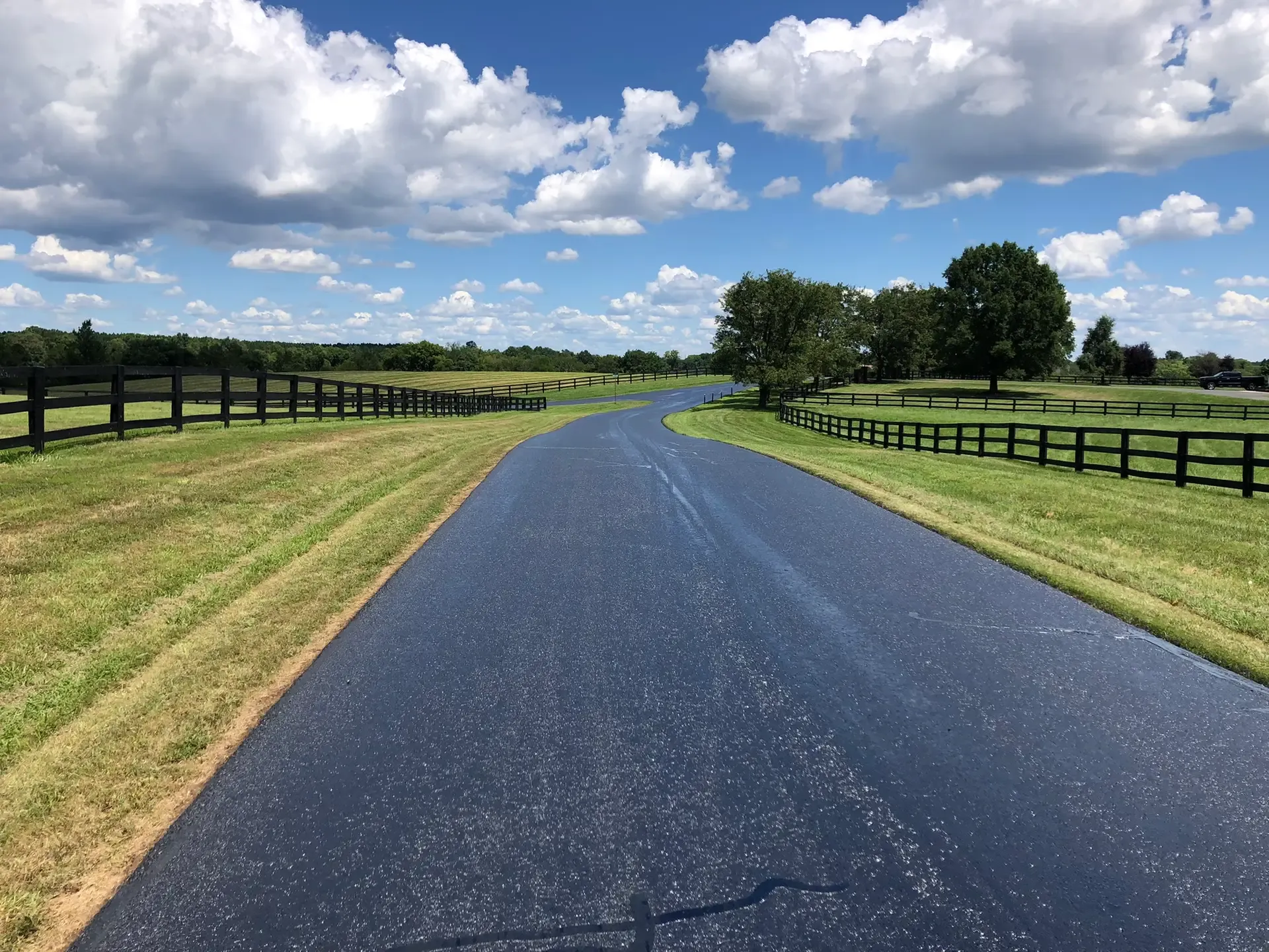 Freshly sealed rural county road running between fenced farm fields.