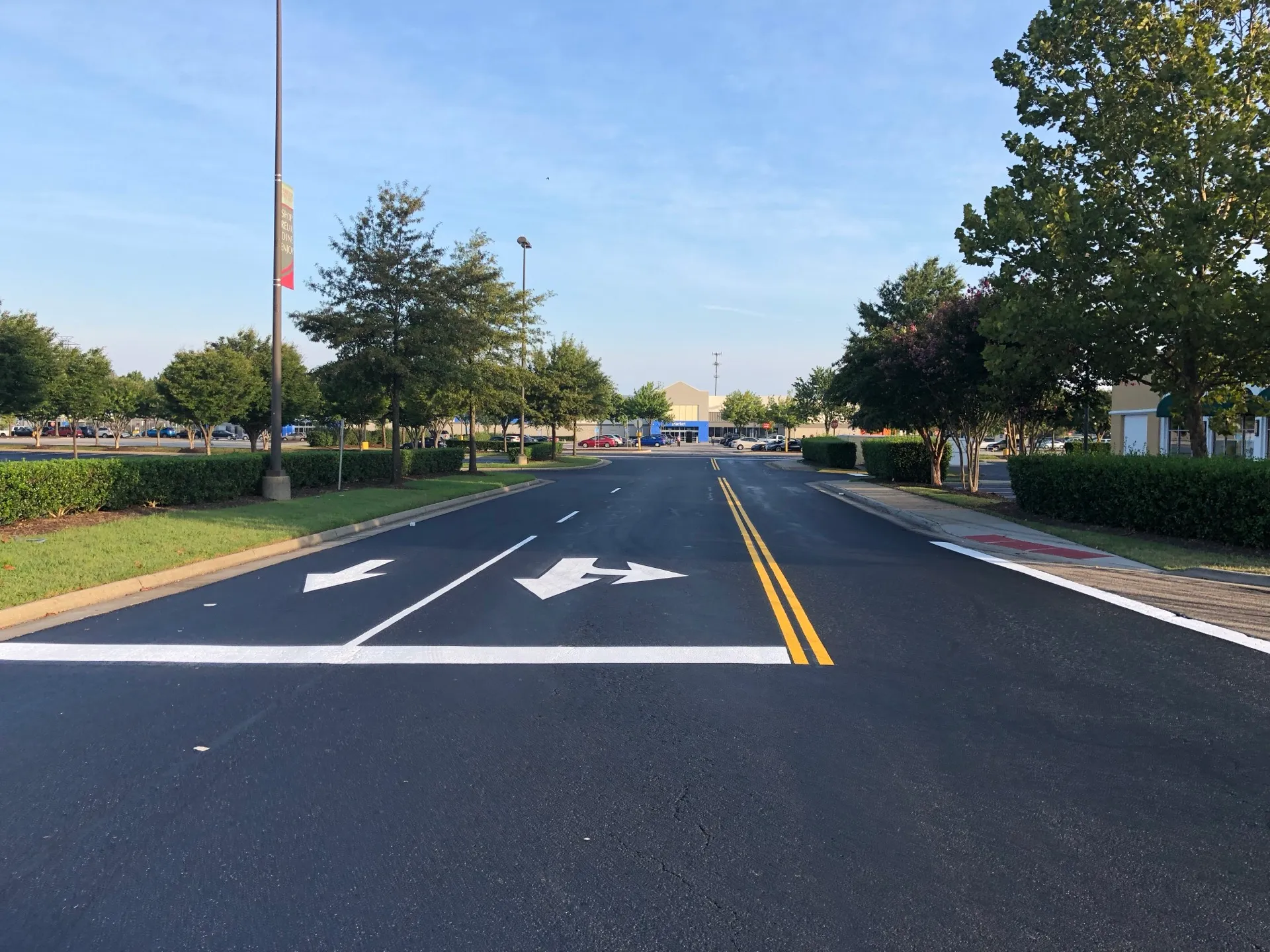 Freshly sealed shopping-center drive lane with crisp lane arrows and storefronts in the background.