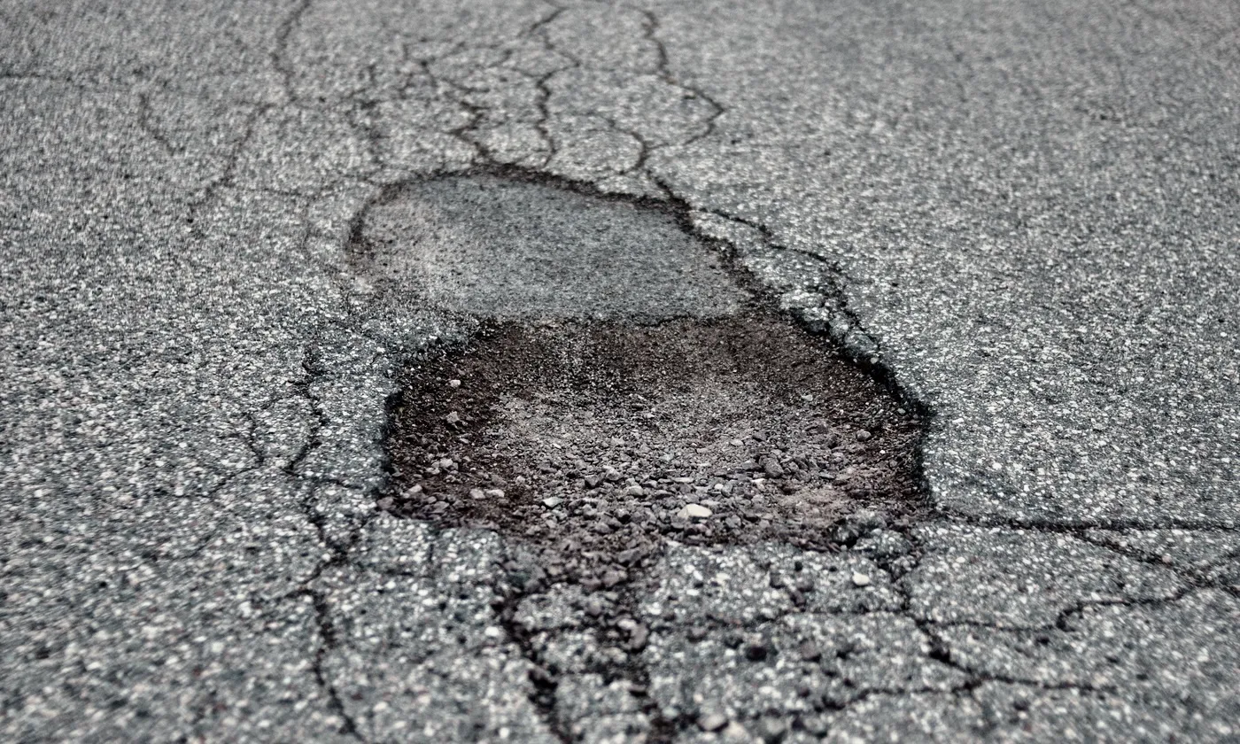 Close-up of a pothole where cracked, untreated asphalt has broken apart