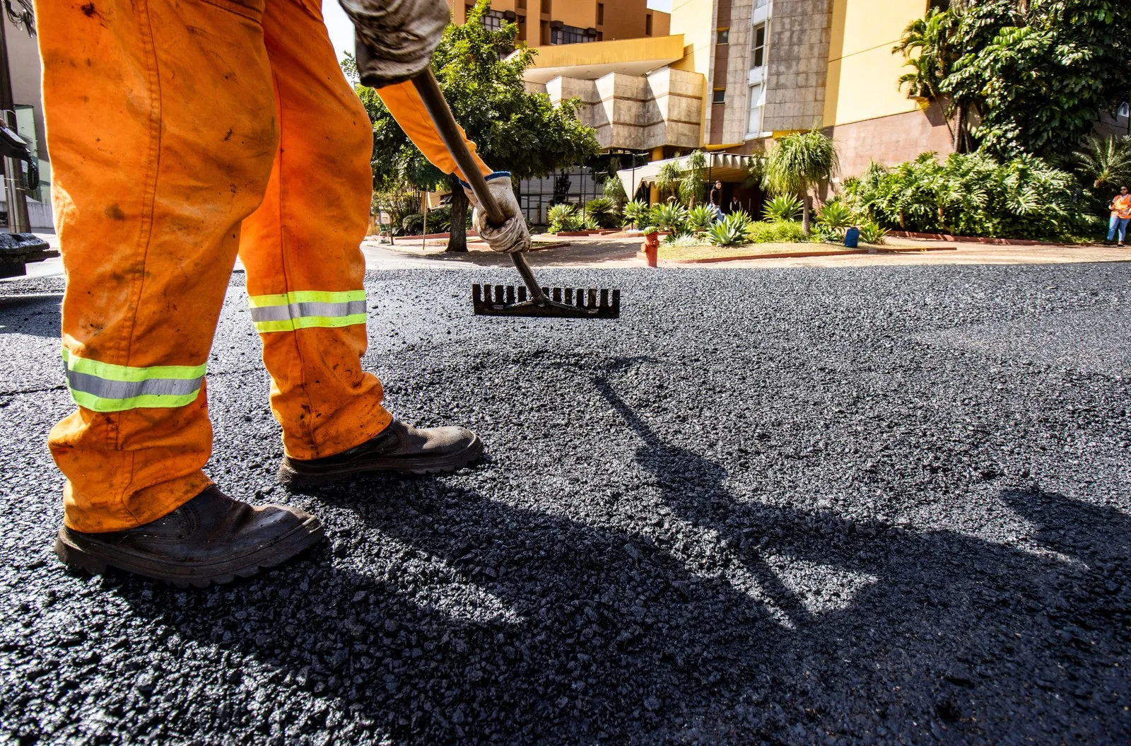 A paving crew worker spreading fresh asphalt with a wide squeegee